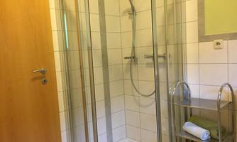 A modern bathroom with a glass shower. On the right, there is a shelf with towels in different colors.