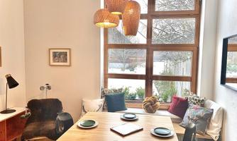 A modern dining room with a large table and atmospheric lighting. Large windows offer a view of the nature outside.