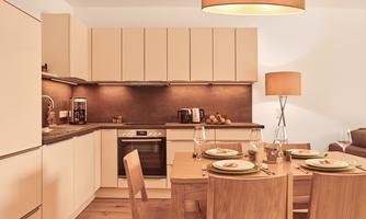 A modern kitchen with light furniture and wooden details. The dining area is elegantly set with dishes and glasses.