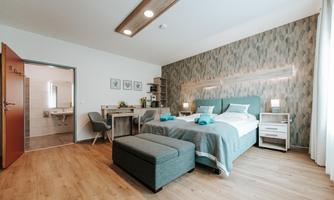 A modern bedroom with a large double bed and stylish furniture. The room features natural wooden elements and is bright and inviting.