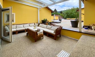 A cozy terrace with a modern seating area and a table. The walls are painted in a sunny yellow, and the space is bright and inviting.