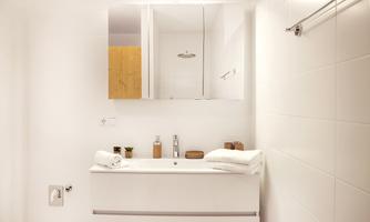 A modern bathroom with white tiles and a stylish sink. The minimalist decor includes towels and small plants.