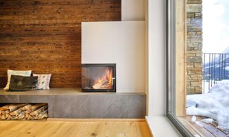 A cozy living space with a modern fireplace and wooden shelves. A snowy landscape is visible through a large window.