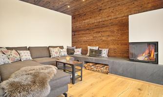 A cozy living room with a gray sofa and colorful cushions. There is a fireplace and wood paneling on the wall.