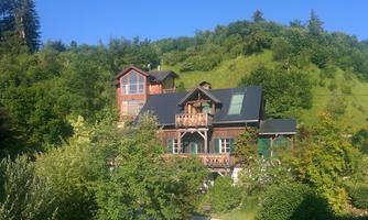 A charming wooden house amidst lush green trees. The building is surrounded by a gentle hill and radiates a cozy atmosphere.