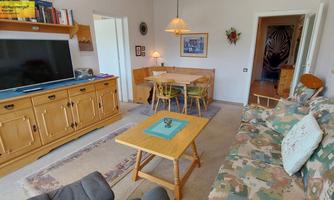 A cozy living room with a comfortable couch and a wooden cabinet. The room has a dining table and a large television.