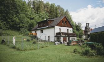 A cozy house surrounded by green nature and trees. The garden is well-maintained and there is a fenced area.
