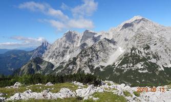 An impressive mountain landscape with high peaks and a clear sky. Green meadows and rocks in the foreground complement the natural beauty of the surroundings.