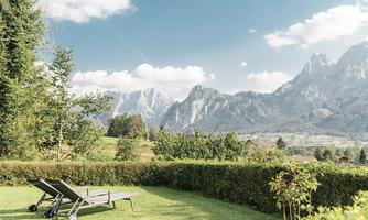 A quiet garden with loungers and a wonderful view of the mountains. The sky is blue and there are some clouds.