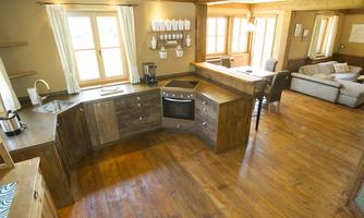 A modern kitchen with wooden surfaces and an open room design. The space is bright and inviting with large windows and a cozy seating area.