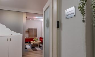 A modern room with an inviting atmosphere. The door leads into a bright area with furniture and plants.