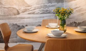 A modern table with wooden chairs, set with white bowls. In the center is a vase with yellow flowers.