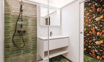 A modern bathroom with a glass shower cabin and green tiles. The walls are decorated with floral patterns.