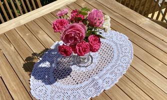 A beautiful bouquet of pink roses is standing in a glass vase on a nostalgic doily. The wooden table gives the arrangement a warm atmosphere.