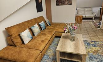 A cozy living room with a brown sofa and a wooden table. On the table sits a vase with flowers, and the room has a modern, inviting character.