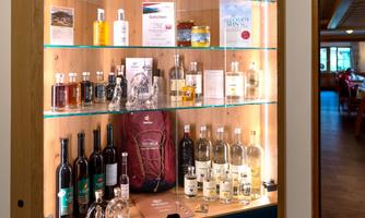 A wooden shelf with illuminated contents, showcasing various bottles and products. Among them are wines, oils, and care products.