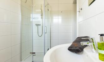 A modern bathroom with a glass shower and a sink. On the shelf, there is a towel and toiletries.