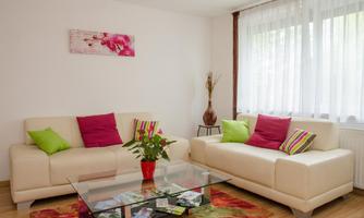 A modern living room with two beige sofas and colorful cushions. A glass table stands in the middle, surrounded by a colorful rug.
