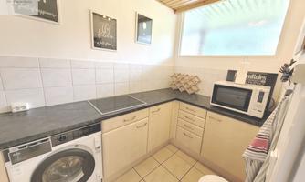 A modern laundry room with a washing machine, a refrigerator, and a microwave. The walls are bright and there are some decorative pictures.