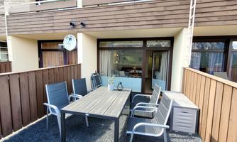 A cozy balcony with a table and chairs. In the background, there are windows and modern wooden paneling.