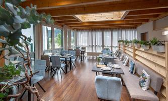A bright and modern restaurant with large windows and wooden ceilings. The tables are elegantly decorated and there are plants in the room's design.