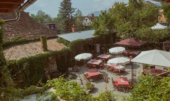 An inviting garden with red tables and umbrellas. Surrounded by green plants and a cozy atmosphere.
