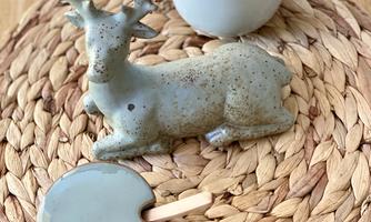 A rustic arrangement with a ceramic deer, a small bowl, and a jug. All objects are placed on a woven coaster.