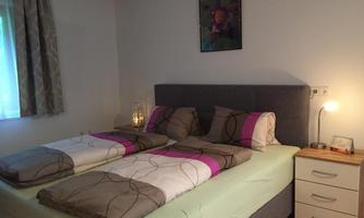 A comfortable bedroom with a double bed and colorful bedspreads. Next to the bed is a nightstand and a window with curtains.