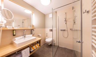 A modern bathroom with a glass shower and an elegant sink. The bright walls and the wooden shelf create a pleasant atmosphere.