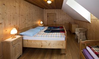 A cozy bedroom in the attic with wooden walls. There are two beds, nightstands, and soft lighting.