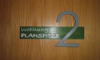 A sign with the inscription "Apartment Planspitze 2". It is made of wood and displays the apartment number 2.