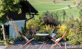 A beautiful outdoor area with two lounge chairs and a table. In the background, there is a green landscape with trees.