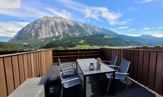 <p>A cozy balcony with a table and chairs. In the background, the majestic Grimming rises under a clear sky.</p>