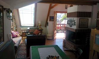 A cozy living room with a fireplace and a seating area. Plenty of daylight comes in through the windows and the door leads to a balcony.