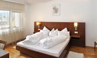 A bright and modern bedroom with a double bed and wooden floor. The windows let in plenty of daylight and the walls are painted in neutral colors.