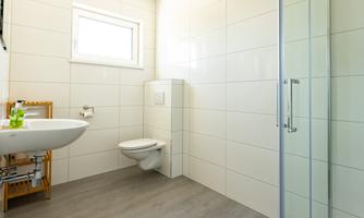 A modern bathroom with bright tiles and a shower. There is a sink and a toilet, well lit by a window.