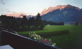 A picturesque landscape with mountains in the background and lush green fields in the foreground. The sky displays soft colors of the sunset.