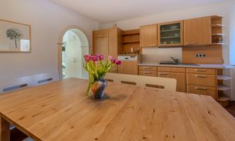 A modern kitchen with wooden cabinets and a large table. On the table, there is a vase with fresh tulips.