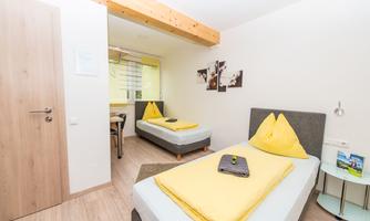 A cozy room with two single beds and yellow bedspreads. The decor is modern and bright, with wooden details and a desk.