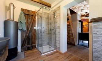 A modern bathroom with a glass shower and a rustic wood detail. The floor is made of light wood and the walls have a natural stone look.
