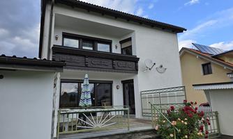 A modern house with a balcony and floral decorations. The sky is partly cloudy and the surroundings appear calm.