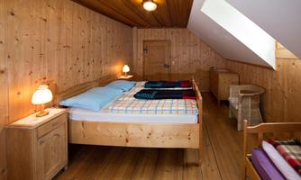 A cozy bedroom with wood paneling and a double bed. There are two nightstands with lamps and a wicker chair.