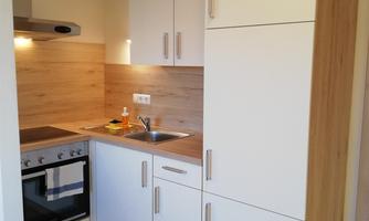 A modern kitchen with white cabinets and wooden surfaces. It is well-equipped with a stove, sink, and worktop.