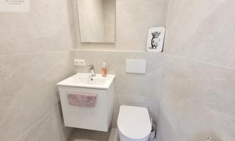 A modern bathroom with bright tiles and a white toilet. A small washbasin cabinet with a mirror and a decorative drawing on the wall.