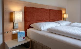 A cozy bedroom with a comfortable double bed and warm light sources. A book lies on the nightstand.