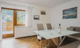 A modern dining room with a glass table and elegant chairs. The windows let in a lot of natural light and offer a view of the surrounding landscape.