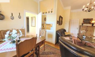 A cozy living room with a dining table and comfortable sofas. The walls are painted light and decorated, giving the room an inviting atmosphere.