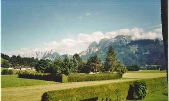 A picturesque landscape with green meadows and mountains in the background. The sky is clear with some clouds.