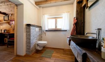 A modern bathroom with wooden beams and a large window. The decor is simple and elegant, featuring a combination of wood and stone.