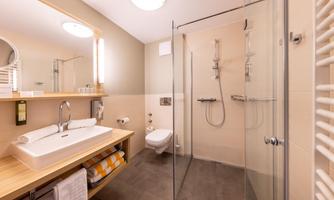 A modern bathroom with a glass shower and a wooden vanity. The walls are light, and the furnishings are functional and stylish.